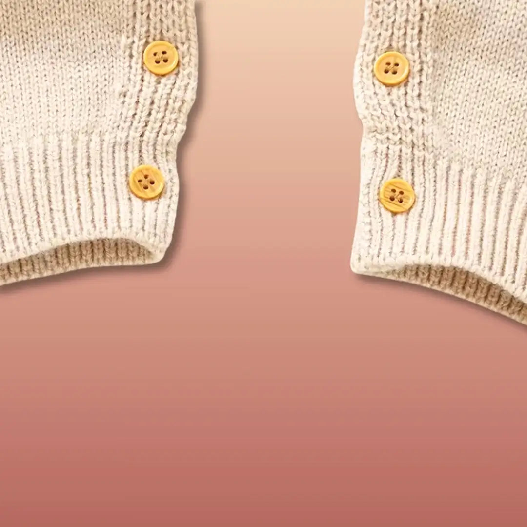 Cozy knit cuffs with button details on a baby romper against a warm autumn background.