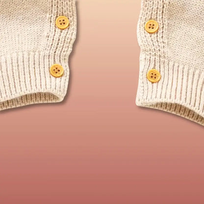 Cozy knit cuffs with button details on a baby romper against a warm autumn background.