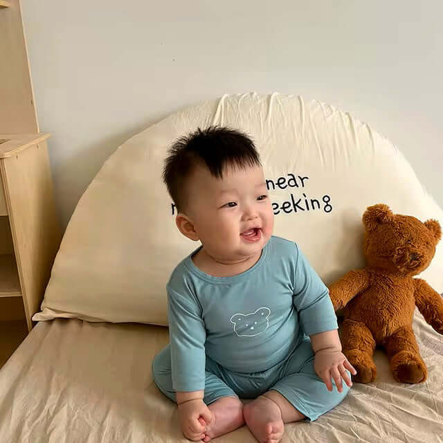 Baby in Snuggle Bear Pajamas sitting on bed with teddy bear, wearing soft and stretchy 2-piece set with playful bear print.