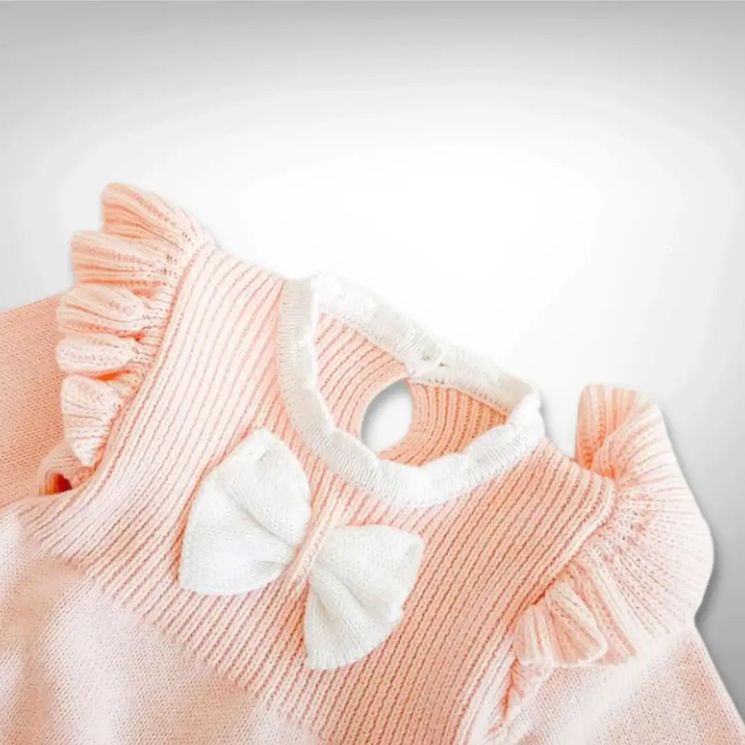 Soft blush knit romper with ruffle sleeves and white bow detail for babies 3-24 months, perfect for special occasions.