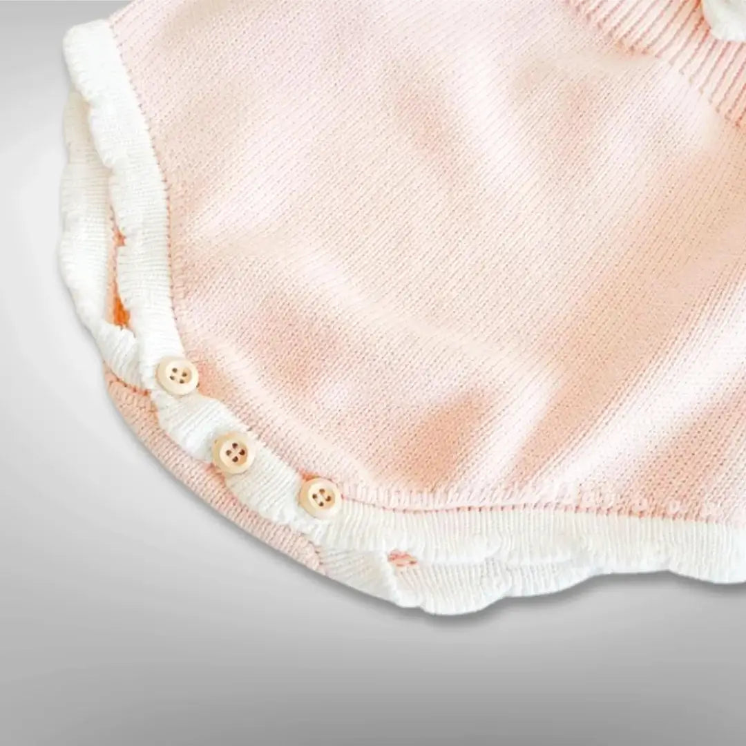 Close-up of blush knit romper with wooden button details for babies, from Ballerina Dreams collection, showing soft fabric and ruffle accents.