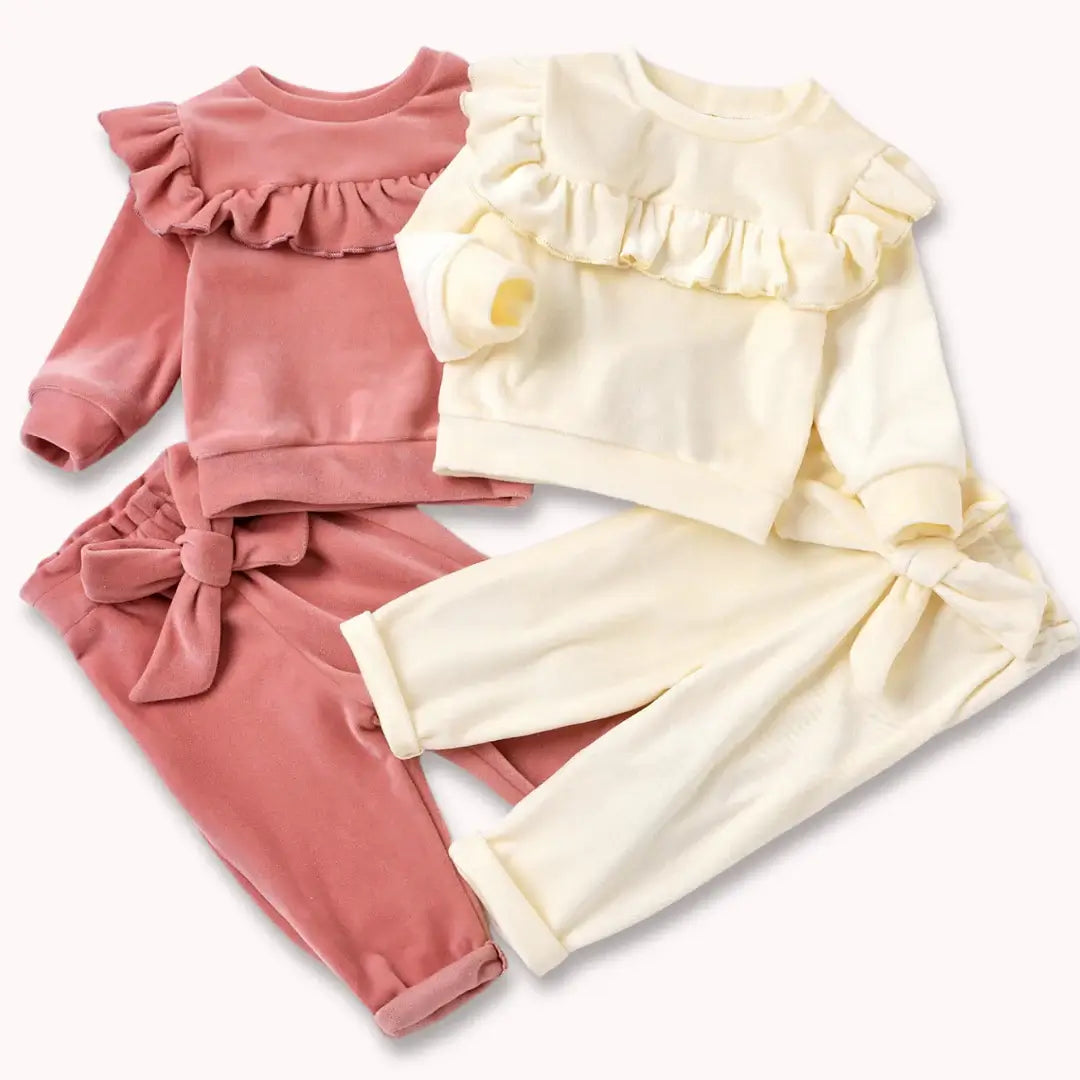 Velvet baby outfits in blush and snow with ruffle tops and bow-tie pants, perfect for warmth and elegance.