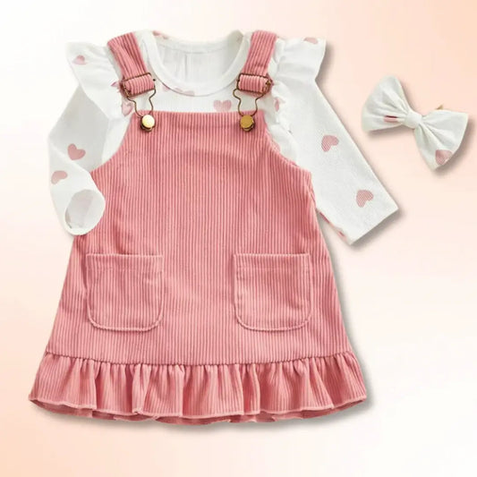 Blush pink corduroy pinafore set with heart-print bodysuit and matching bow for infants (3-18M).