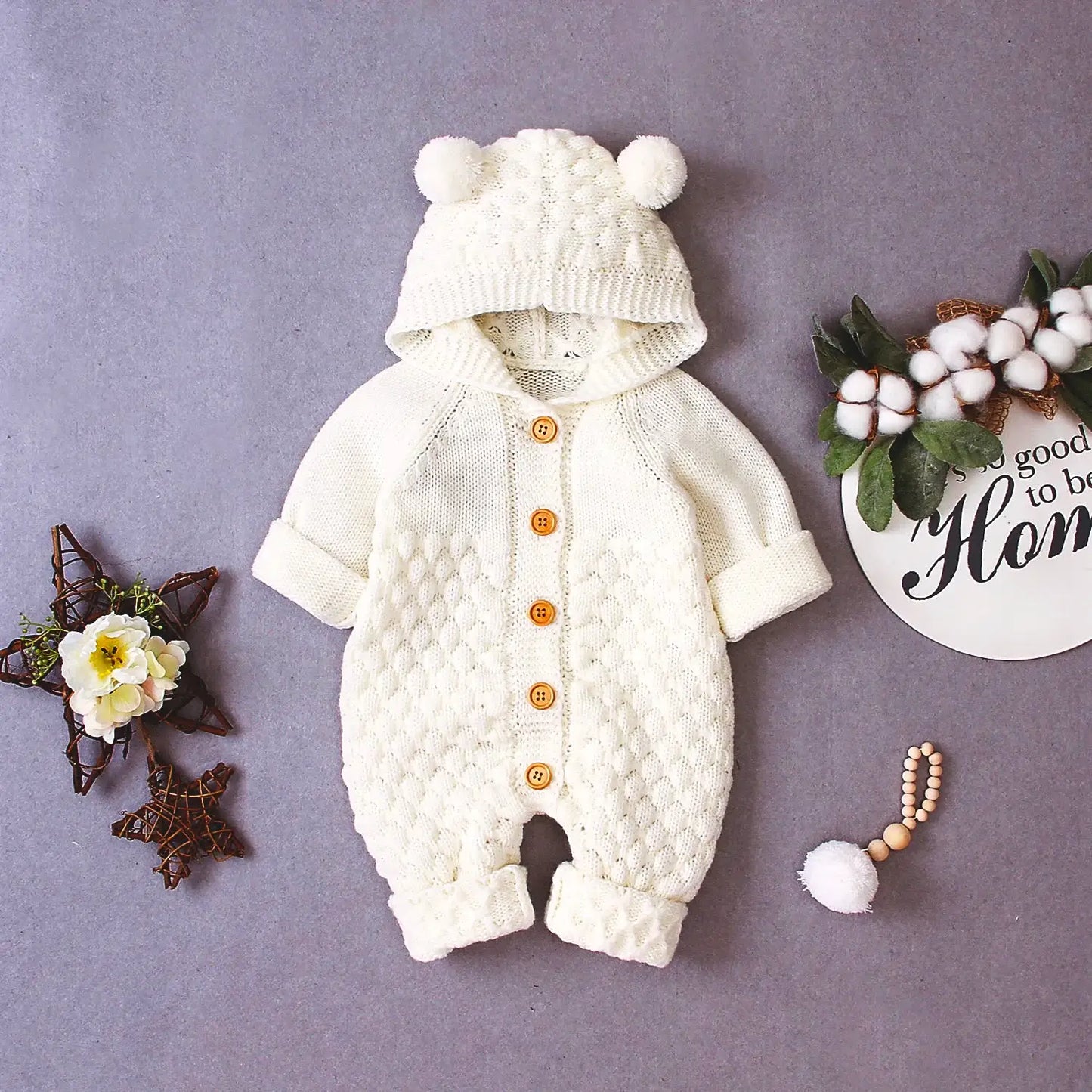 Cuddle Bear Knit Romper in cream with hood and bear ears for babies 0-18 months, cozy and warm knit jumpsuit on display with decor items