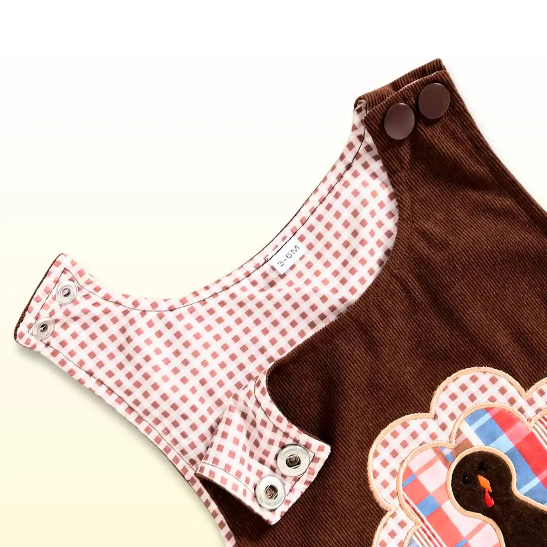 Turkey appliqué corduroy baby overalls with checkered lining and button snaps for easy changes, perfect for Thanksgiving.