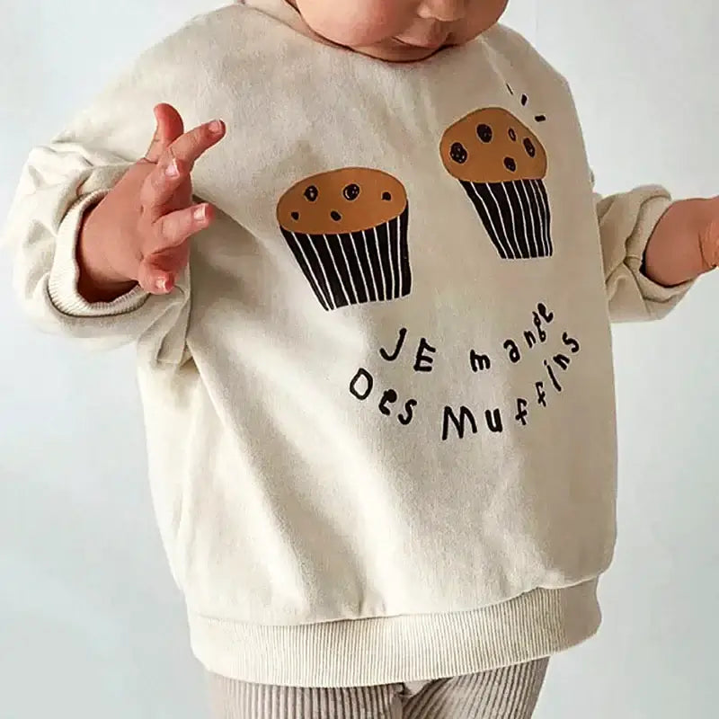 Child wearing "Je Mange Des Muffin" casual sweatshirt with cute muffin design, perfect for ages 18M-6Y, indulging in cozy style.