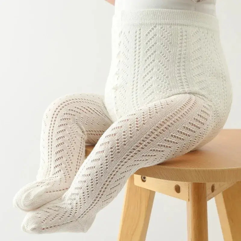 Baby wearing hollow out mesh tights in white for comfort and style, sitting on a wooden stool.