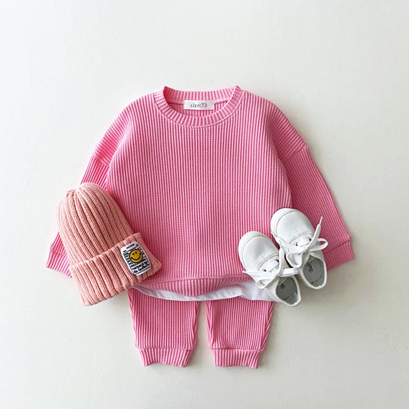 Trendy pink waffle-knit toddler sweatshirt with matching pants, beanie, and white sneakers for stylish comfort.