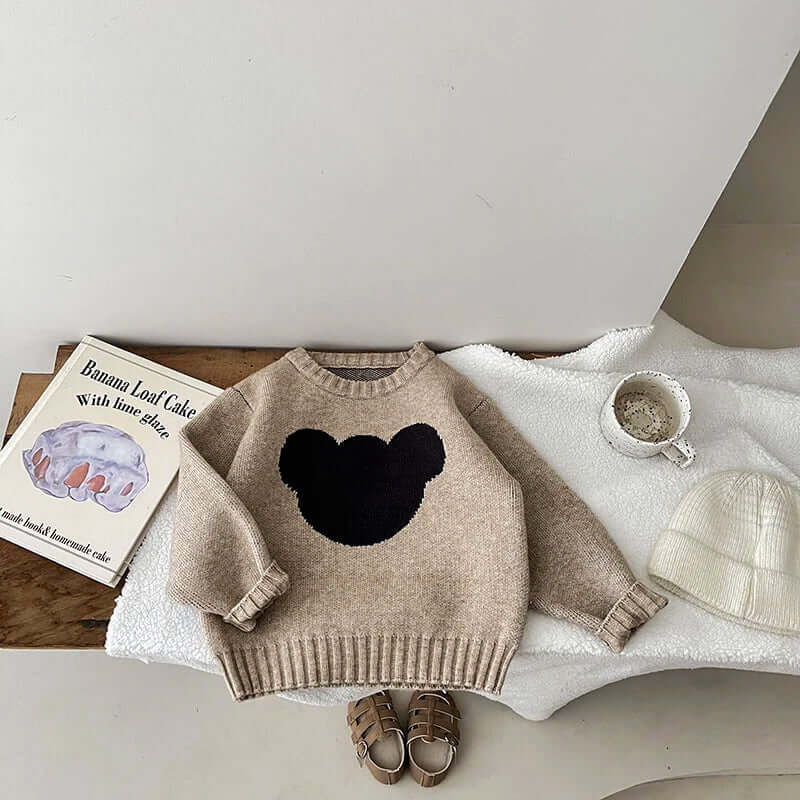 Beary Cute Cotton Sweater with cartoon bear design laying on a table next to baby shoes, a hat, and a book